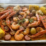Cajun seafood boil with garlic butter sauce, crab legs, shrimp, sausage, corn, potatoes, and lemon on a sheet pan.